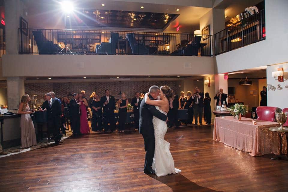 bride and groom having first dance in center of room with guests watching behind them